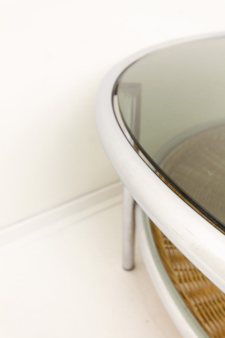 Vintage ronde salontafel met verchroomd frame, glazen blad en rotan krantengedeelte